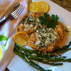 a white plate topped with chicken, asparagus and lemons next to a fork