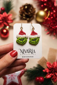 a pair of green heart shaped earrings with santa hats on them sitting in front of christmas decorations