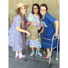 three women standing next to each other with a walker in front of a building and smiling at the camera