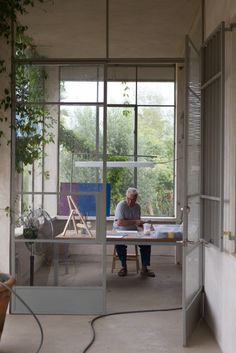 a man sitting at a table in front of a glass wall with plants growing on it