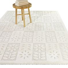 a table with books on top of it next to a white rug and wooden stool