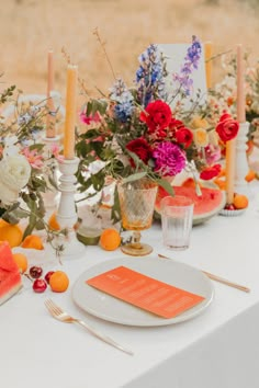 the table is set with watermelon, oranges and other colorful floral arrangements