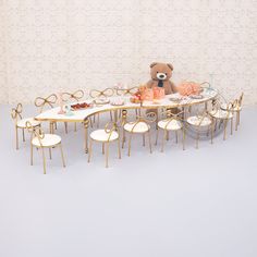 a teddy bear sitting at a table with many chairs and plates on top of it