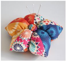 a bunch of colorful pillows sitting on top of each other with pins stuck in them