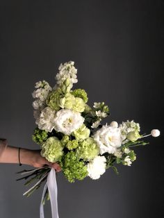 a bouquet of white and green flowers being held by a woman's arm with her hand