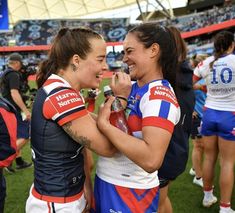 two female rugby players standing next to each other on a field with fans in the background