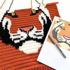 a crocheted tiger rug next to a pen and paper