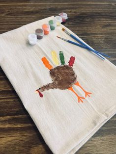 a turkey handprinted on a white towel with paint and crayons next to it