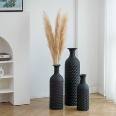 three black vases sitting on top of a wooden floor next to a book shelf