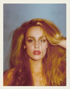 a woman with long red hair has her hands on her head and is looking at the camera