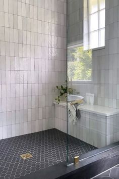 a white tiled bathroom with black flooring and glass shower door, window above the sink