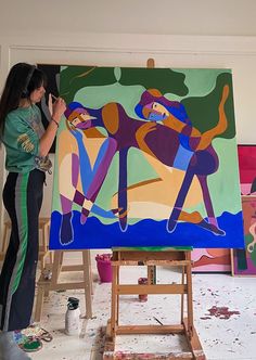 a woman is painting on an easel in front of some other art work,