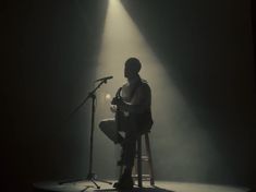 a man sitting in front of a microphone on top of a stool next to a microphone