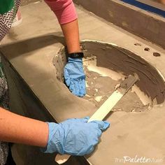 a woman in blue gloves is working on a piece of concrete