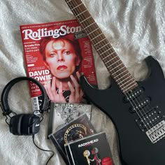 a guitar, headphones and magazine on a bed