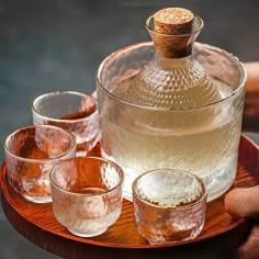 a glass pitcher and four glasses on a wooden platter with a bottle in the middle