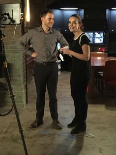 a man and woman standing next to each other in front of a camera on a tripod