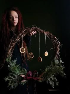 a woman holding a wreath with ornaments hanging from it's sides in front of her face