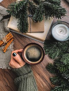 a woman holding a cup of coffee on top of a wooden table next to candles