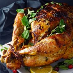 a roasted chicken on a plate with lemons and herbs