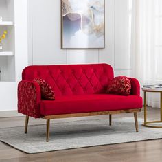 a red couch sitting on top of a wooden floor next to a white rug and table