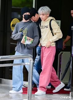 two young men are walking out of an airport with their backs to each other and one is wearing a face mask