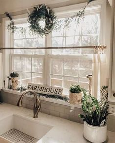 a kitchen sink under a window with a farmhouse sign hanging above it and plants on the windowsill