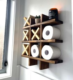 two wooden shelves with rolls of toilet paper hanging on the wall next to a window