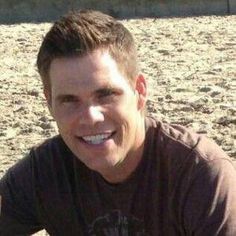 a man sitting on the beach with his surfboard in hand and smiling at the camera