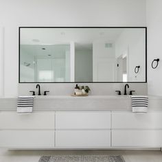 a white bathroom with two sinks and large mirrors on the wall above them is shown