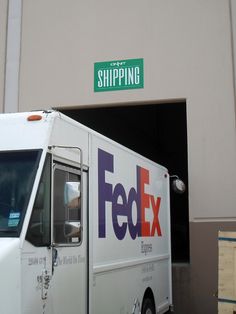 a fed ex delivery truck parked in front of a shipping building with the door open