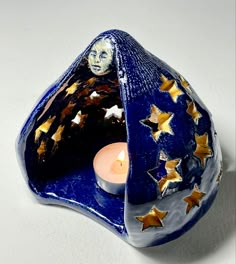 a blue candle holder with gold stars and a face in the center, on a white surface