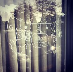 a window with the word boo on it in front of some curtains and trees outside