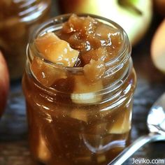 an apple jam in a glass jar with spoons next to it on a table