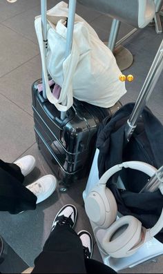 luggage and headphones sitting on the floor in an airport terminal with people's feet propped up next to them