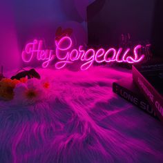 a neon sign that says hey gorgeous on top of a fur covered bed with flowers