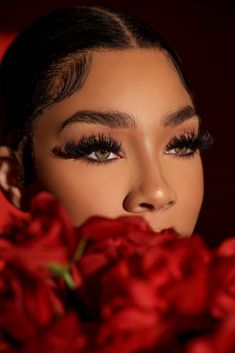 a woman with long lashes and red roses in front of her face is looking at the camera