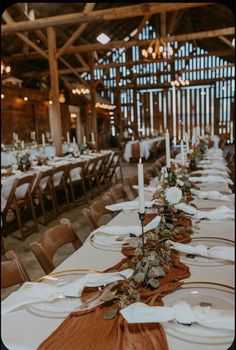 a long table set with white plates and place settings for an elegant wedding reception at the barn