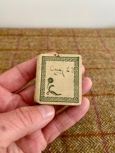 a hand holding a small square brooch with writing on it