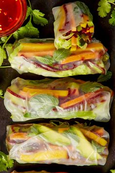 three rolls filled with lettuce, carrots and other veggies next to some ketchup