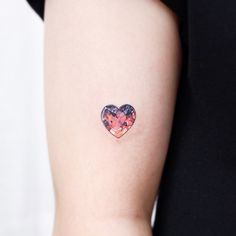 a small heart tattoo on the left side of the right arm, with pink and blue flowers in it