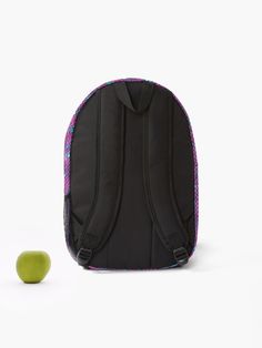 an apple sitting next to a black backpack with pink and green trim on the front