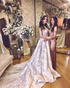 two women standing next to each other in front of a mirror wearing wedding gowns