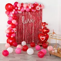 balloons and streamers are on the floor next to a red curtain with love written on it