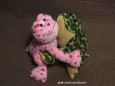 a pink and green frog stuffed animal sitting on top of a brown blanket with polka dots