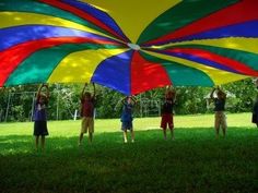 several people standing under a colorful umbrella in the middle of a grassy field with trees behind them