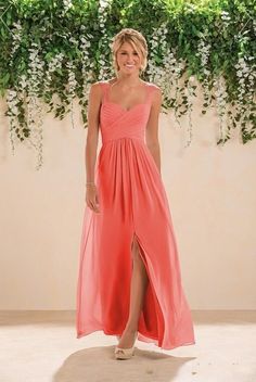 a woman in a coral colored dress standing next to a wall with flowers on it