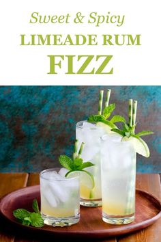 two glasses filled with limeade rum fizz sitting on top of a wooden tray