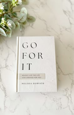 a book sitting on top of a white table next to some green leaves and flowers