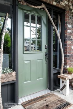 a green front door on a brick building with a tree branch in the foreground